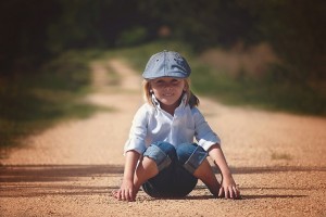 little girl sitting in the middle of a dirt road